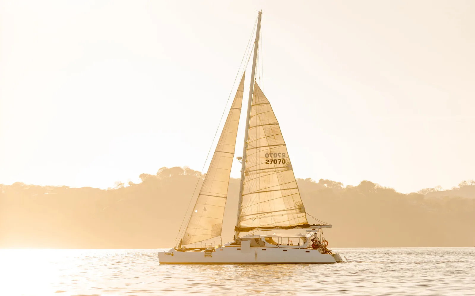 Lohe Lani, an Ocean Club sailing catamaran with sails up in golden evening light off Costa Rica's Pacific coast