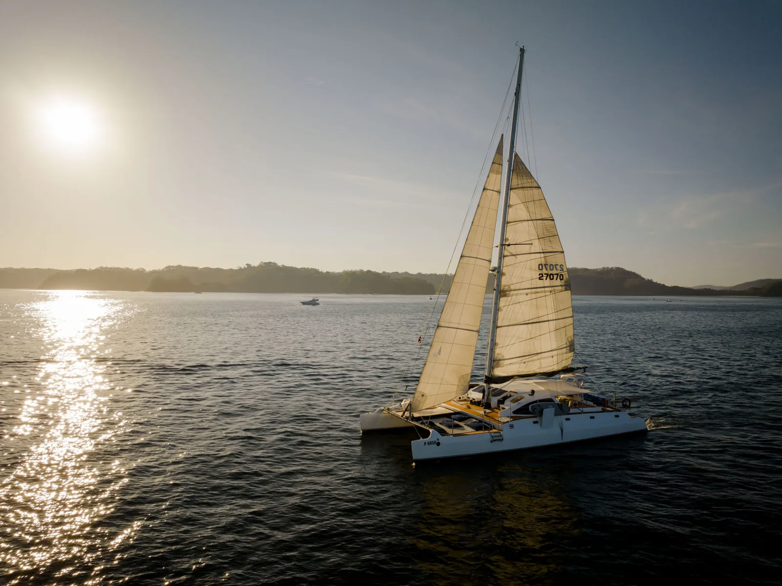 Lohe Lani at anchor at sunset, the sun dropping behind the headland