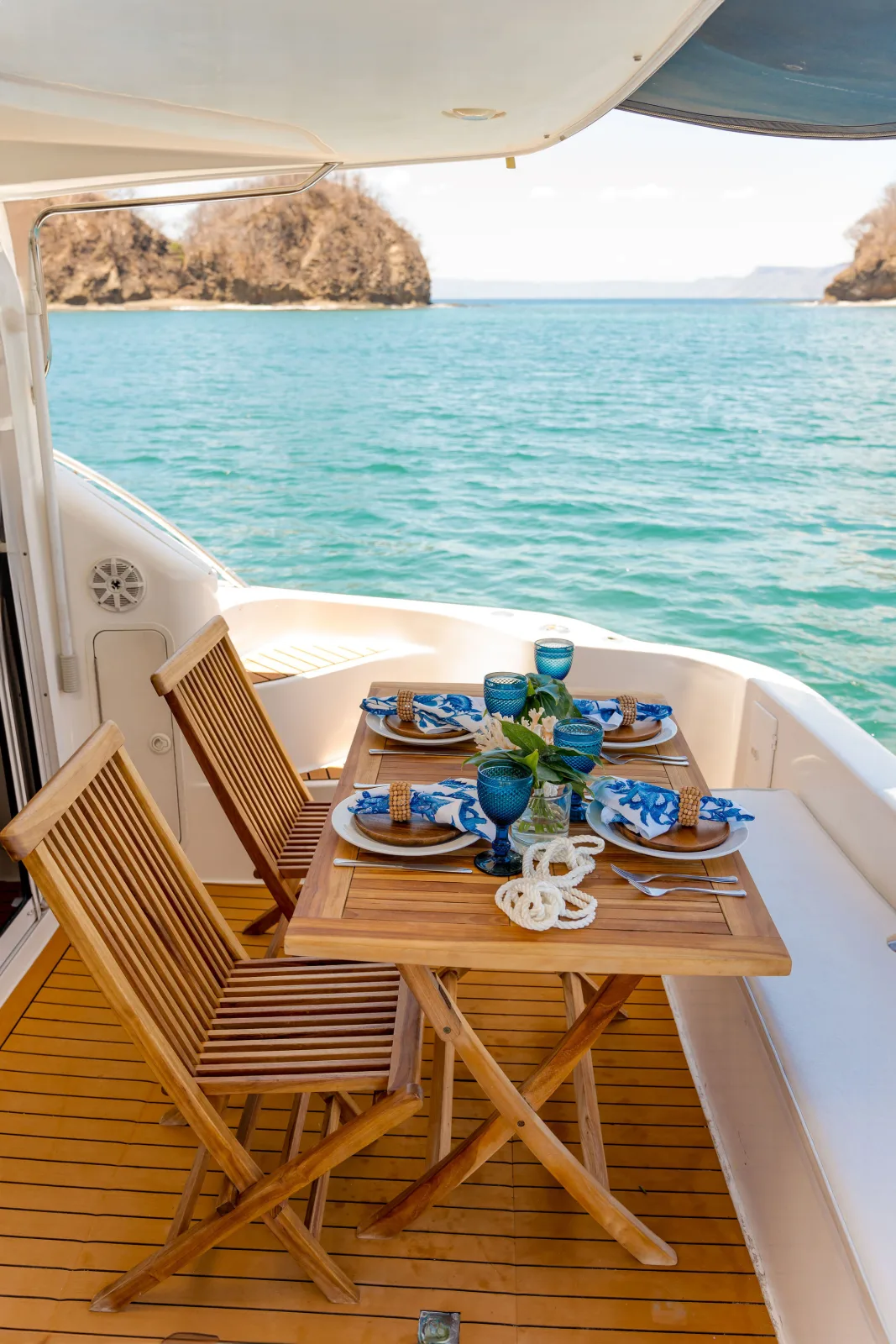 The teak dining table on Sea Ya's aft deck, over turquoise water